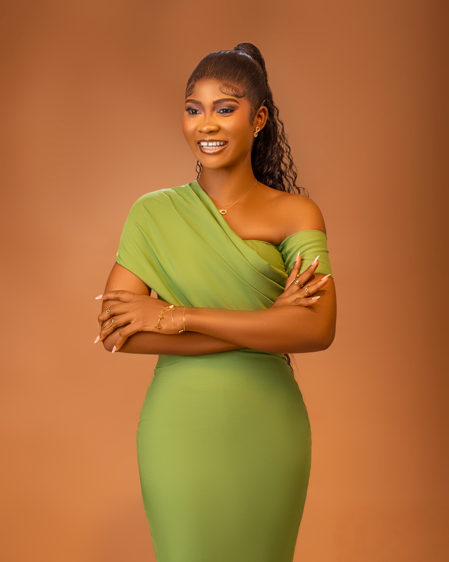 A smiling author and editor in a sage green dress, standing against a warm tan studio backdrop